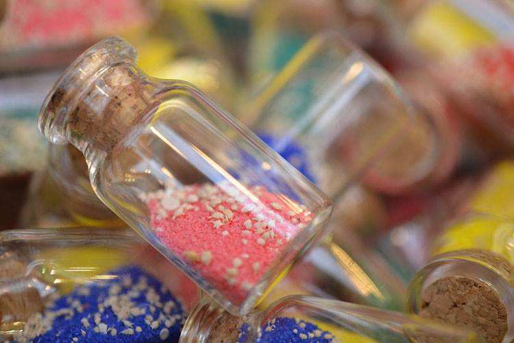 A pile of small glass bottles filled with brightly colored sand and miniature seashells