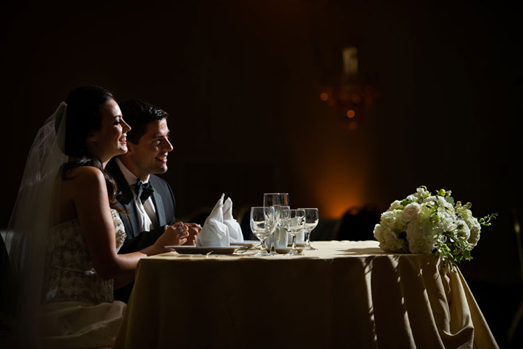 A bride and groom sitting at a wedding table with the lights turned down