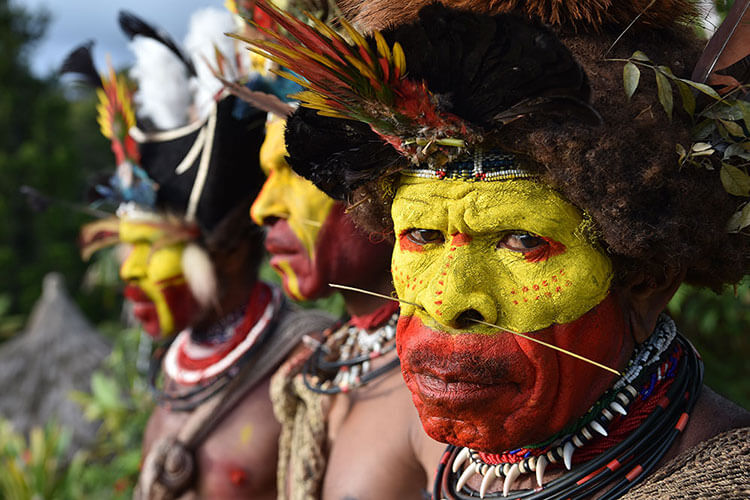 Three tribesmen with their faces painted in bright yellow and red