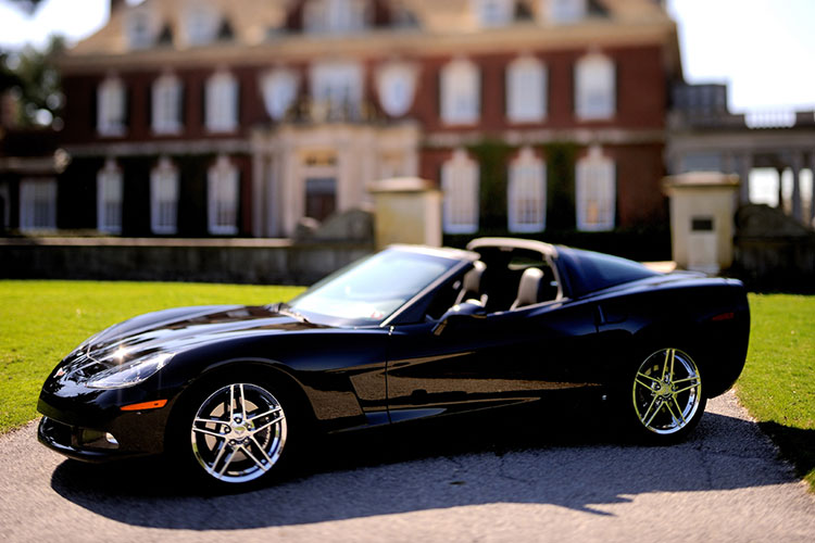 A shiny black sports car sits in front of a large brick house