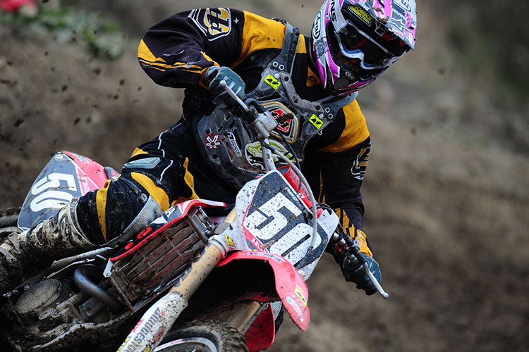 A motocross rider races on a dirt track, flinging up mud