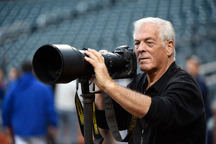 A photographer with a Nikon DSLR and NIKKOR lens inside of a sports stadium