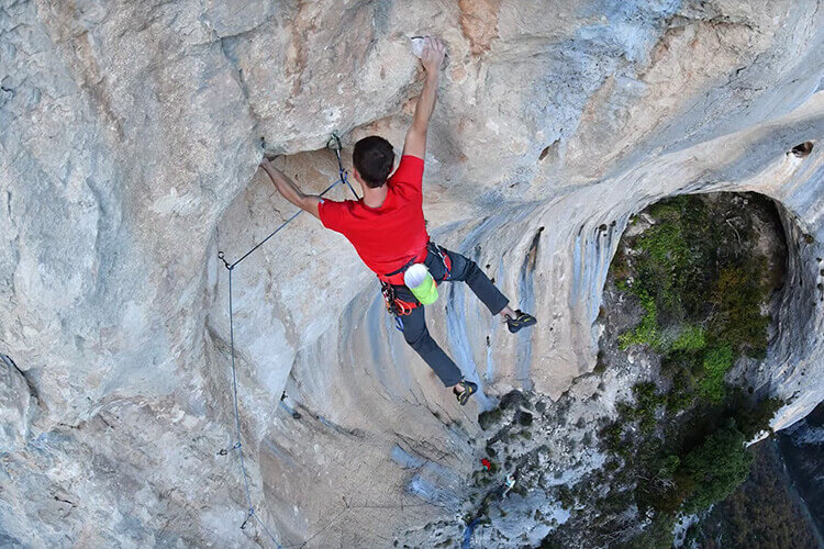 A rock climber hanging on a rock ledge with his hands