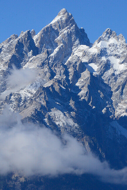 Snowy peaks of a mountain show through the clouds with a bright blue sky in the background