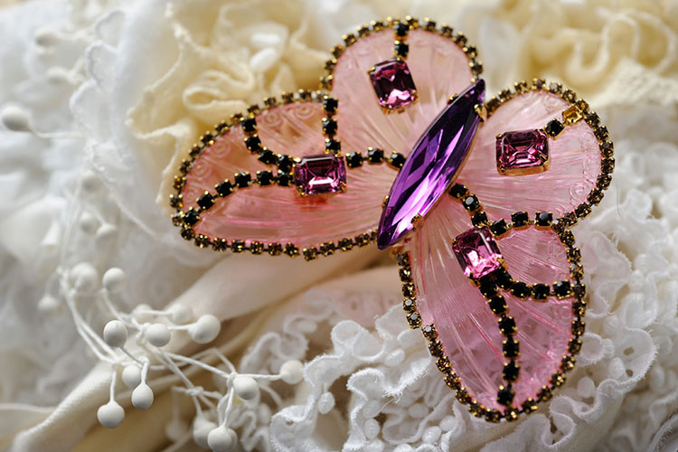 A butterfly shaped brooch with pink and purple jewels rests on white lace