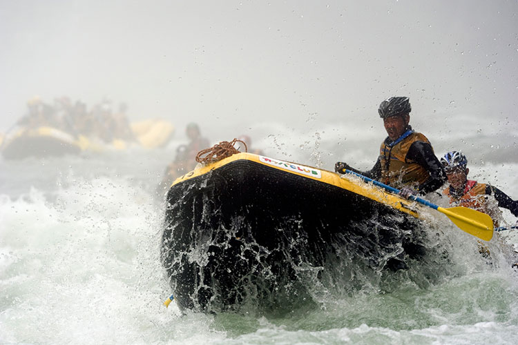 A group of rafters in the foreground paddle though the rapids with other rafts in the background