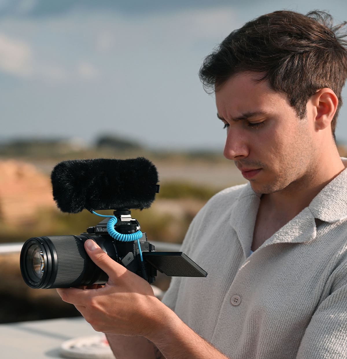 Photo of a man holding the Z f camera with a mic on the hotshoe, looking at the LCD that's flipped out
