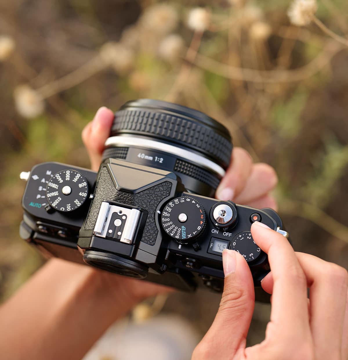 Photo of a person's hands holding a Z f camera and changing dials on the top of the camera body