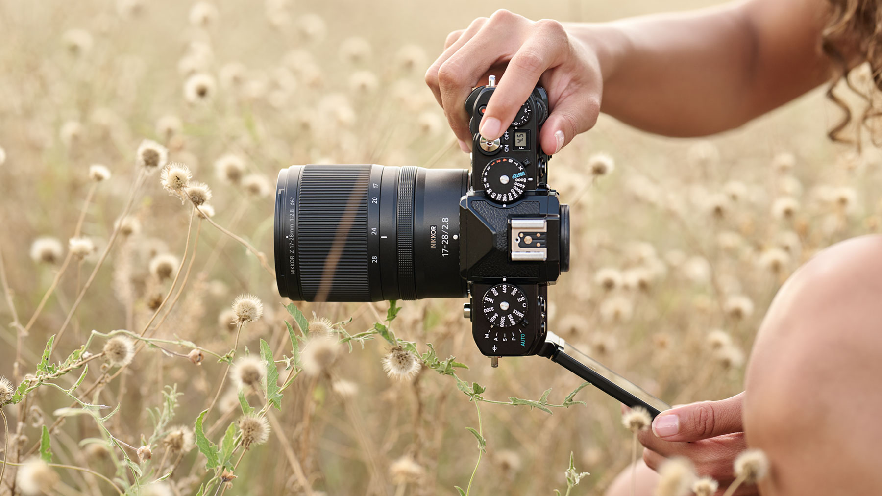 Photo of a person holding the Z f camera and lens, with the LCD flipped out, in a field of out of focus flowers