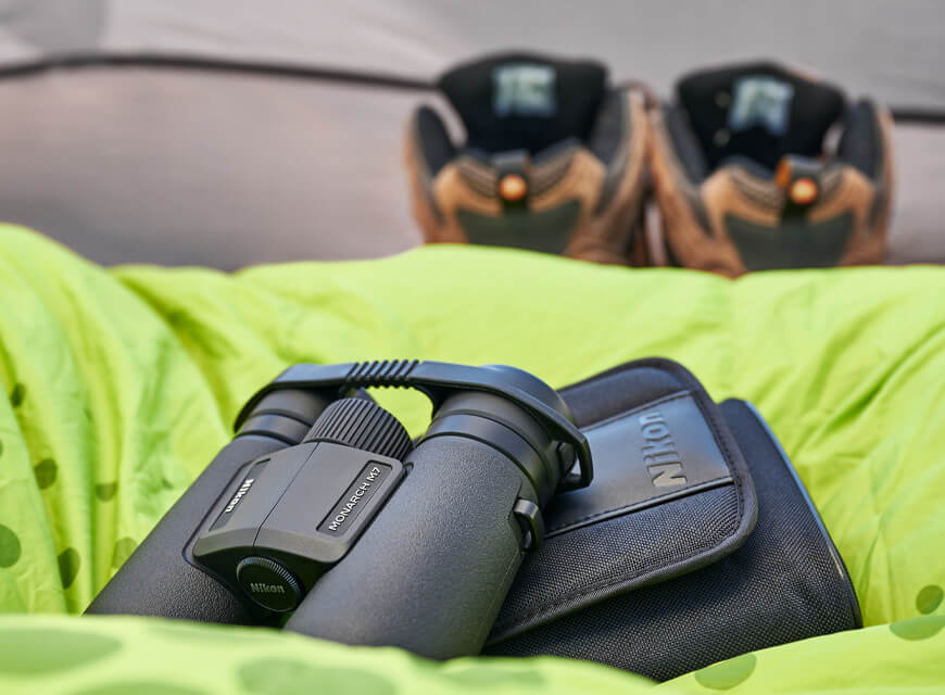 Photo of a pair of Monarch M7 binoculars and case on a green sleeping bag